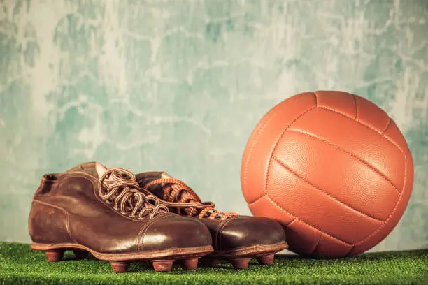 Photo of Retro outdated soccer spike boots and football. Vintage old style filtered photo