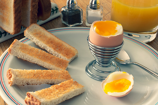 Breakfast, soft boiled egg, toast soldiers, fresh orange juice and salt and pepper.