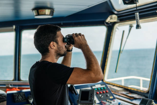 istock Navigational officer lookout on navigation watch looking through binoculars 1054705436
