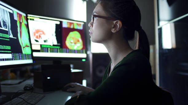 Watching physiology screens Close up stock image of a young asian woman working at a desk with multiple monitors.
She’s studying the moving data & information on the screens which consists of human body scans, MRI & CAT, and scrolling text & numbers. neuroscience stock pictures, royalty-free photos & images