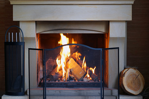 A warm fire in the stone fireplace on a cold night. Warm cozy fireplace with real wood burning in it. Cozy winter concept. Christmas and travel. Christmas backgrounds. Magic burning fireplace.