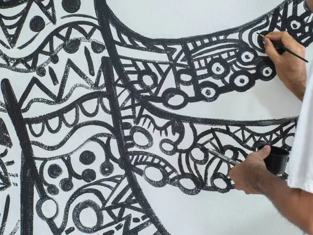 Photo of Closeup artist painting abstract pattern in octopus shape on white cement wall.