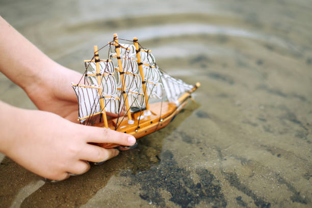 istock child playing with a toy sailing ship by the river, hand closeup 1054745980