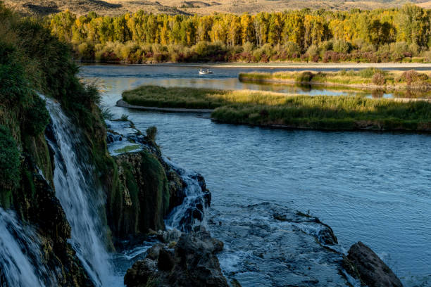 istock Dramatic scene with waterfall and autumn trees as a drift boat passes 1054752526