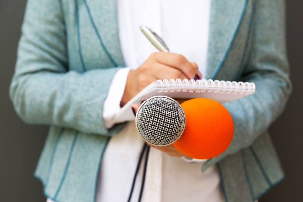 istock Journalist at news conference, holding microphone, writing notes 1054758698