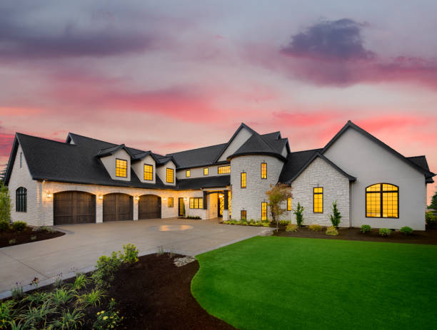 Beautiful luxury home exterior at sunset facade of home with manicured lawn, and backdrop of trees and dark blue sky gable photos stock pictures, royalty-free photos & images