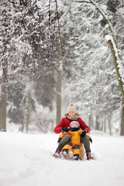 Little boy and mother sliding in the park during a snowfall