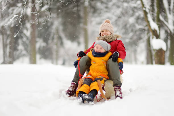 istock Little boy and mother sliding in the park during a snowfall 1054784982