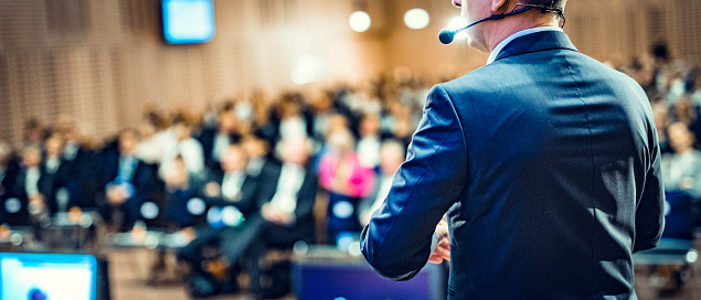 Rear view of a businessman entrepreneur giving a lecture to a sold-out crowd in a lecture hall.