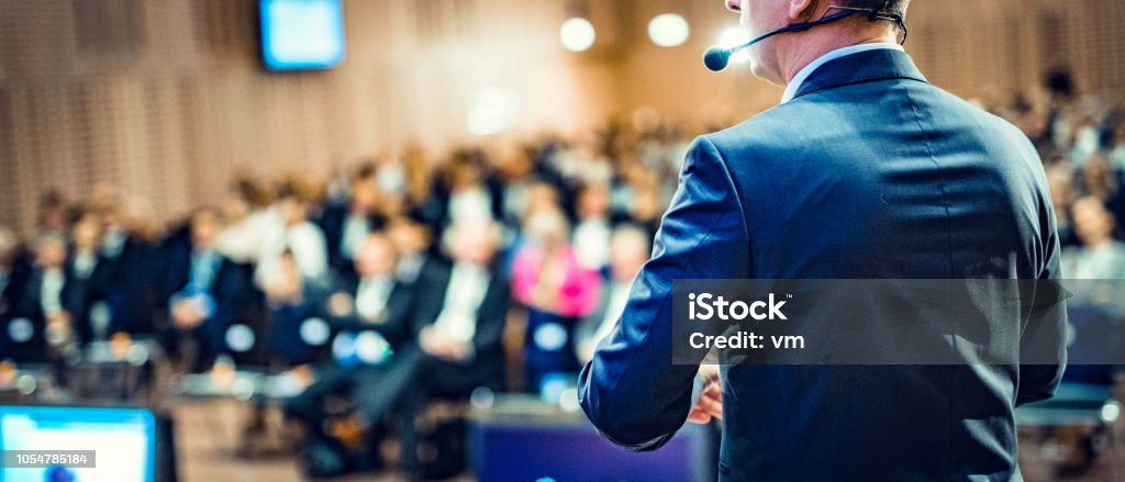 Rear view of a motivational coach giving a speech Rear view of a businessman entrepreneur giving a lecture to a sold-out crowd in a lecture hall. Public Speaker Stock Photo