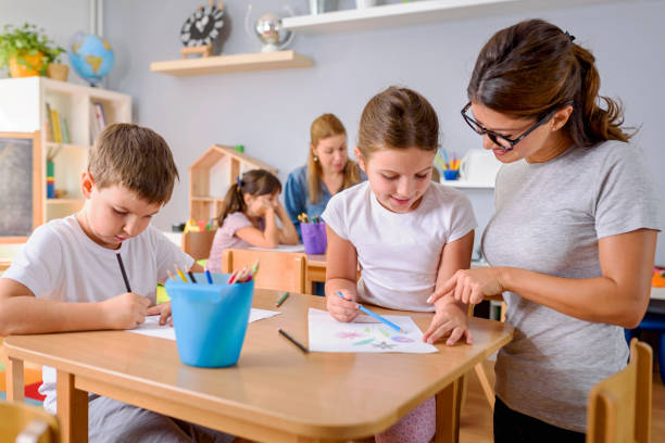 istock Children drawing with smiling preschool teacher assisting them 1054792408
