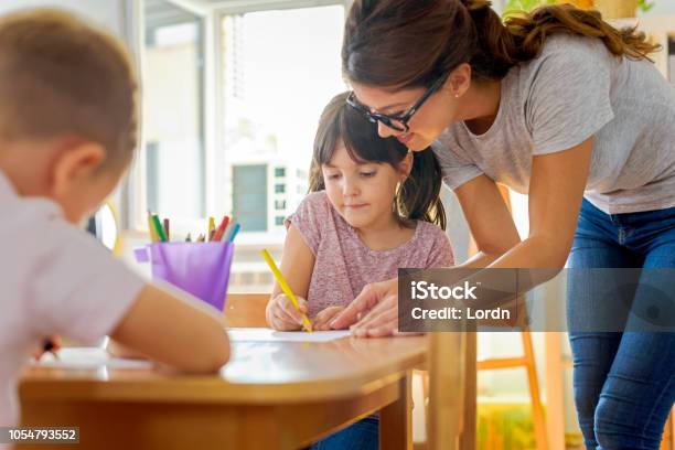 Children Drawing With Smiling Preschool Teacher Assisting Them Stock Photo - Download Image Now