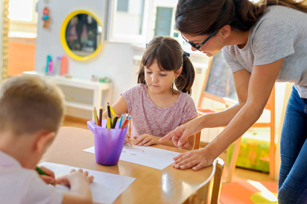 istock Children drawing with smiling preschool teacher assisting them 1054793766