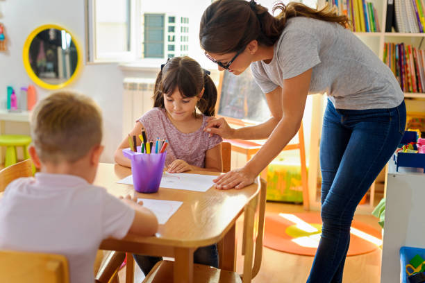 istock Children drawing with smiling preschool teacher assisting them 1054793818