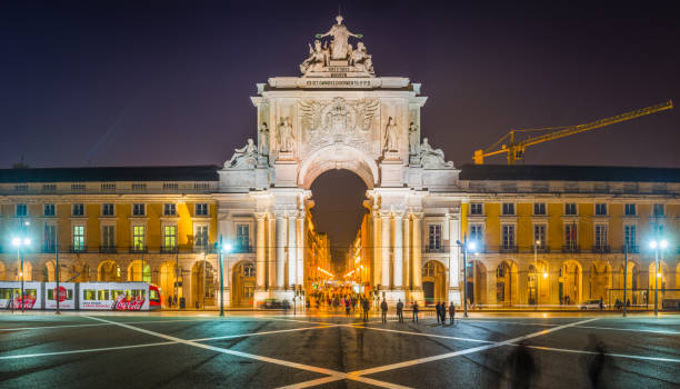 Spotlights illuminating the Rua Augusta Arch after sunset, the historic landmark overlooking the crowds of tourists in the Praca do Comercio in the heart of Lisbon, Portugal’s vibrant capital city.