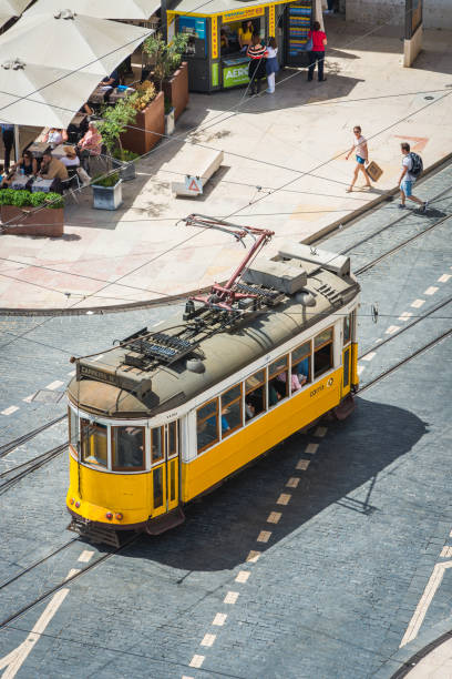 Aerial view over the cobbles of the Praca do Comercio to an iconic yellow tram and tourists in the heart of Lisbon, Portugal’s vibrant capital city.