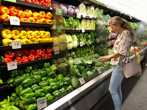 Cheerful woman selecting fresh vegetables (broccoli) in a supermarket. Horizontal composition. Side view. Indoors.