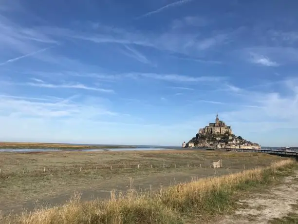 In this Photo we can sea Mont Saint Michel during a sunny day. A little number of CloudKit fill the blue sky over the island and yellow-brown ground create a wonderful contrast.