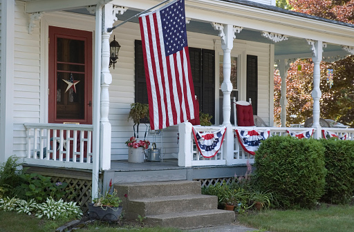 An old Colonial house in Massachusetts is decorated with red, white, and blue bunting and the American Flag to celebrate the nation's Birthday