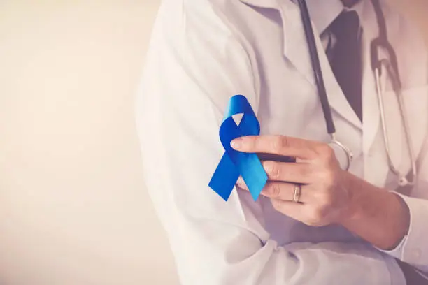 Doctor hands holding blue ribbon,  diabetes and Colorectal Cancer Awareness