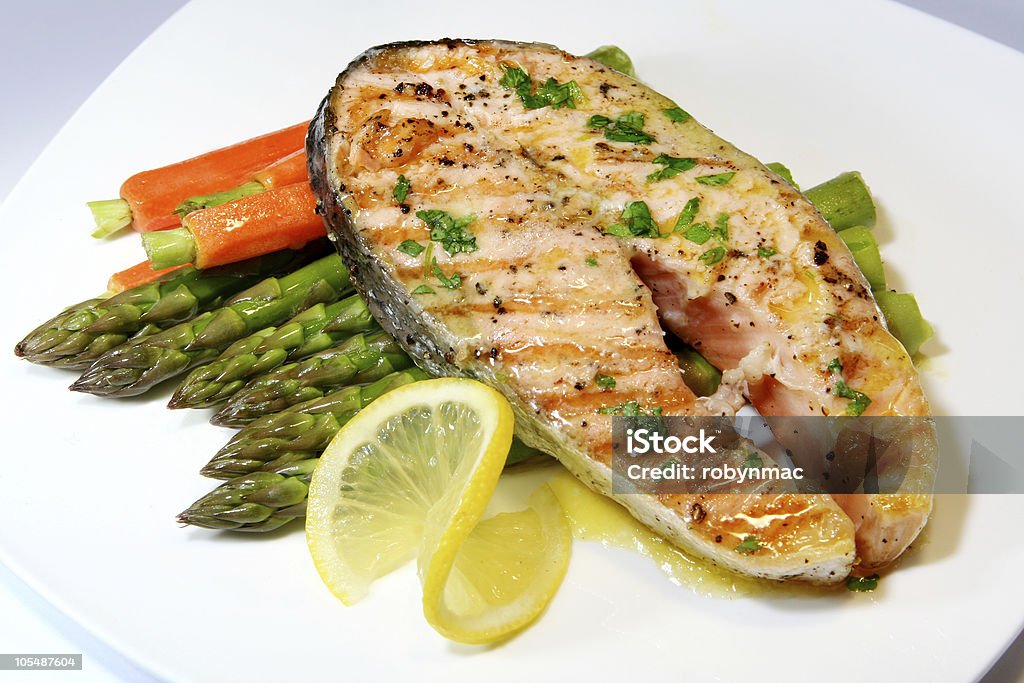 A piece of grilled salmon with asparagus on a white plate Salmon Dinner ~ grilled salmon cutlet with asparagus and baby potatoes, and a butter and parsley sauce.  Please see: Butter Stock Photo