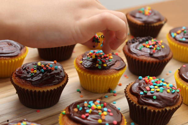 enfants dans la cuisine ! détail de la main d’un enfant mettre sprinkes sur un petit gâteau - cupcake chocolate icing candy photos et images de collection