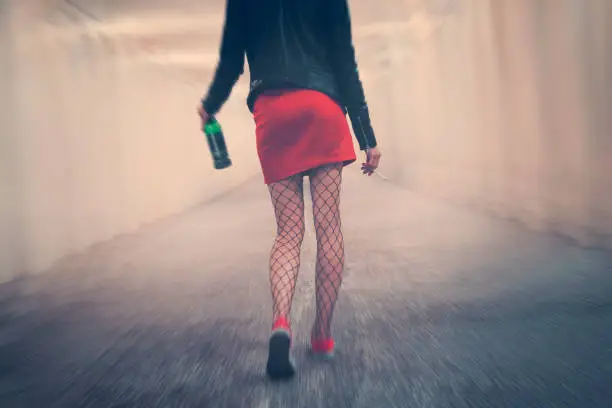 drunk woman with cigarette and bottle goes into distance along corridor stumbling and falling. Young girl in red skirt tights walk away. concept of alcoholism bad habits. Blur effect showing dizziness