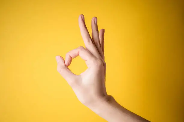 woman hand pointing up okay, yes, accepting hand sign to the side, studio isolated on yellow background