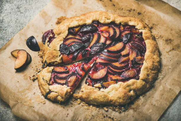 Round plum galetta cake on baking paper over concrete background Round plum galetta sweet cake on baking paper over grey concrete background, selective focus, horizontal composition. Seasonal Fall or Autumn dessert crostata stock pictures, royalty-free photos & images
