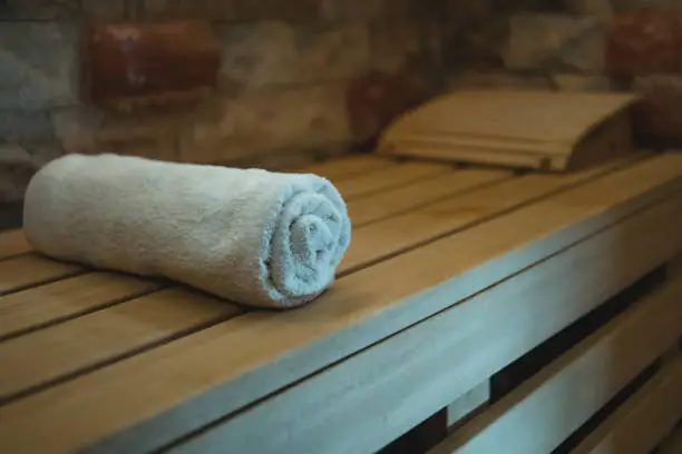 An individual cotton towel on a wooden bench prepared for a sauna client. Comfortable classical steam sauna amenities. Client-oriented sauna with first-class facilities. Wellness procedures in a bath