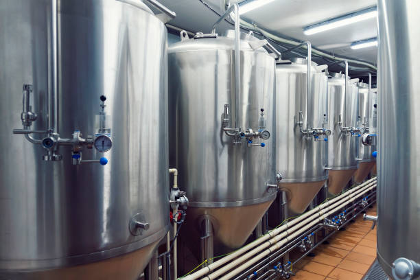 linien der metall-tanks in moderne brauerei. shopfloor mit brauereianlagen. herstellbare prozess der brewage. modus der bierproduktion. brauen. innenansicht des modernen bier anlage mit edelstahl-fässern. - brewery beer barley cereal plant stock-fotos und bilder