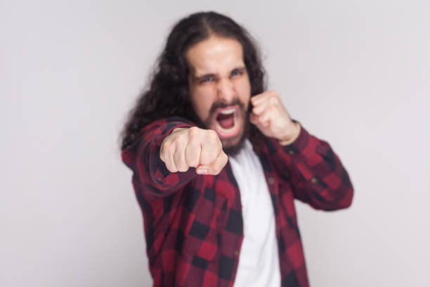 homme en colère qui crie avec barbe et cheveux longs bouclé noirs en casual chemise rouge à carreaux debout, regardant la caméra et s’attaquer à coups de poing de boxe. - beautiful red hair curly hair human hair photos et images de collection