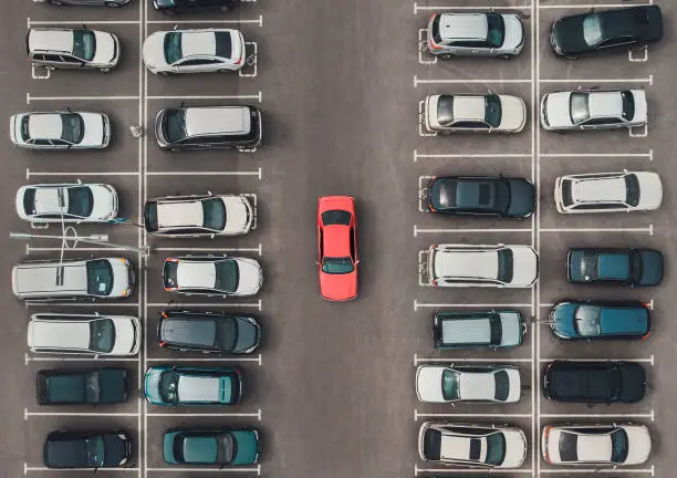Photo of Top view of the crowded Parking lot with quadcopter or drone. Original bright automobile among the grey of mediocre cars. Parking space search, No parking space.