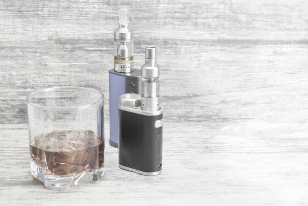 istock Whiskey in a glass with an e-cigarette and liquid for it on a gray stone background 1054915338