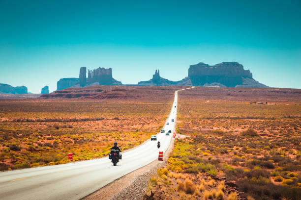 Biker on Monument Valley road at sunset, USA Classic panorama view of motorcyclist on historic U.S. Route 163 running through famous Monument Valley in beautiful golden evening light at sunset in summer, Utah, USA monument valley photos stock pictures, royalty-free photos & images