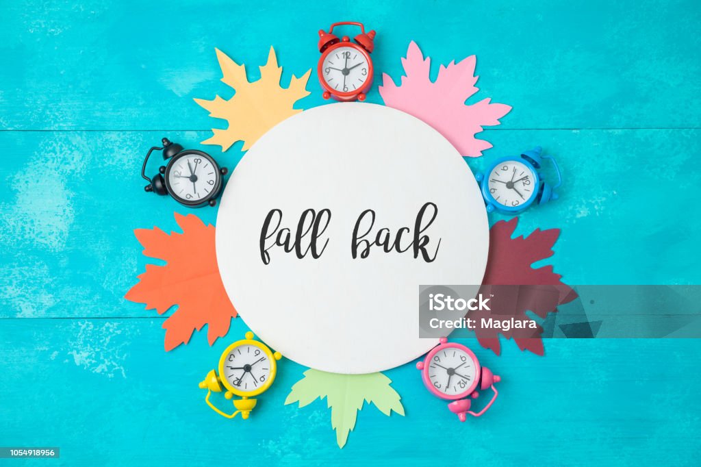 Fall back time change concept. Fall back time change concept. Creative composition with alarm clock, autumn leaves and wooden round board. Top view from above Autumn Stock Photo