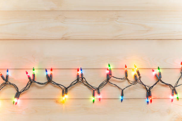istock Christmas light bulbs were turned on or lid on string in multi colours; blue, yellow, red, pink, orange and green on light wooden background at night time, Xmas or new year decoration ornament 1054919718
