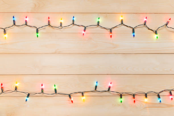 istock Christmas light bulbs were turned on or lid on string in multi colours; blue, yellow, red, pink, orange and green on light wooden background at night time, Xmas or new year decoration ornament 1054919750
