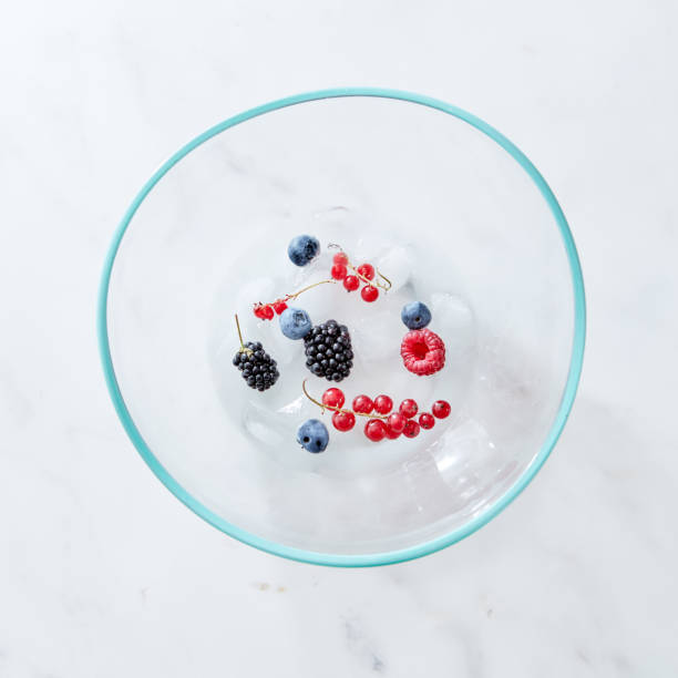 glass bowl with different fresh berries and ice cubes on a gray marble background with space for text. top view - strawberry blueberry raspberry glass imagens e fotografias de stock