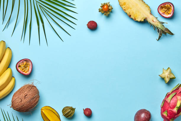 Ripe different exotic fruits, banana, coconut carambola fizalis with a palm leaf on a blue background with space for text. Flat lay