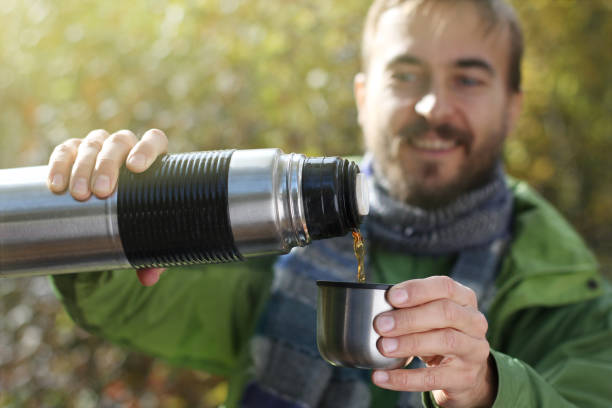 istock man with smile pours a hot drink - tea or coffee from thermos into cup, front view 1054927050