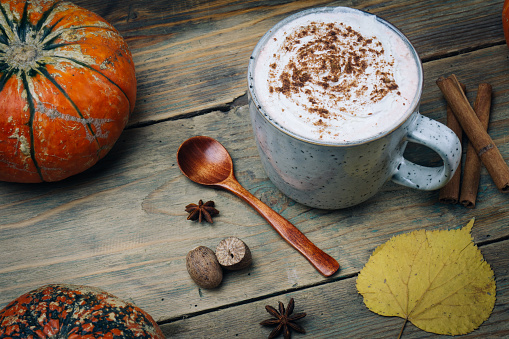 Pumpkin spice latte or coffee with cinnamon. Autumn, fall or winter hot drink. Background with yellow leaves