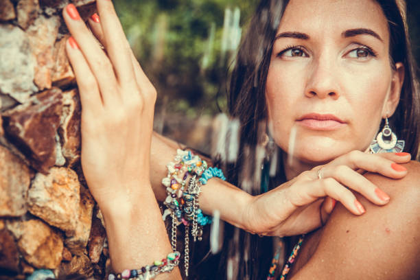 A striking artistic portrait of a beautiful woman with long wavy hair, resting her head on her hand in a thoughtful pose. With her eyes lowered and expression calm yet introspective, the photo evokes themes of contemplation, emotion, and inner thought. Set against a soft green background, this elegant vertical image captures feminine beauty, quiet strength, and emotional depth. Ideal for use in editorials, wellness campaigns, psychology content, or conceptual art.