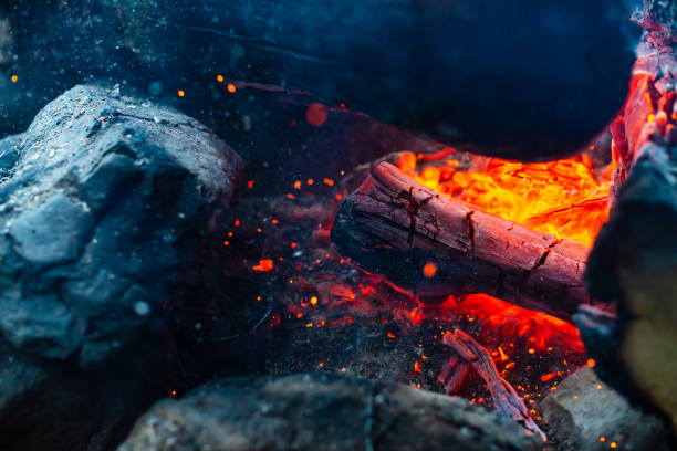 istock Smoldered logs burned in vivid fire close up. Atmospheric background with flame of campfire. Unimaginable detailed image of bonfire from inside with copy space. Whirlwind of smoke and glowing embers. 1054930342