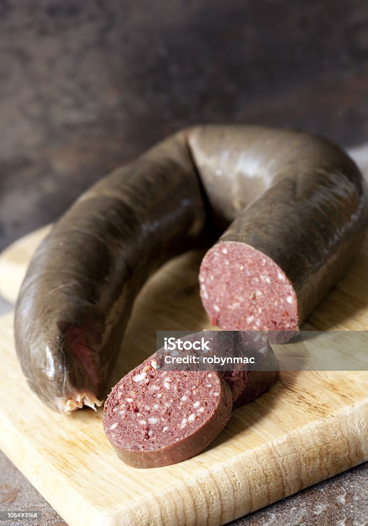 Delicious pudding in a round long shape Black pudding, with cut slices, on chopping board over stone background. Black Pudding Stock Photo