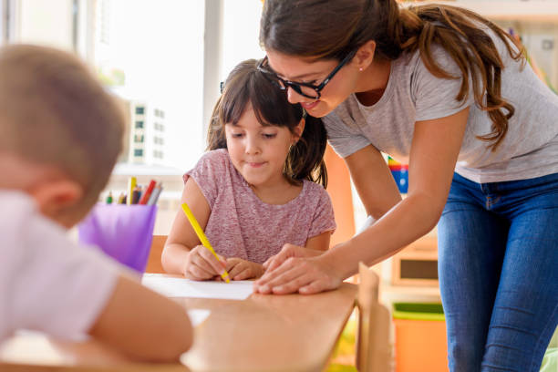 istock Children drawing with smiling preschool teacher assisting them 1054934130