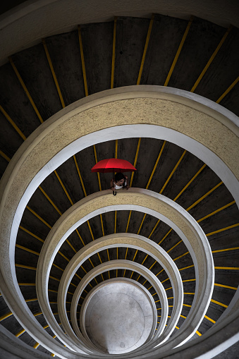 Red Umbrella being held by a mixed race woman looking at camera. Spiral staircase below. Symmetrical. Taken in a pagoda in Chinese Gardens, a public park in Singapore. No fee to enter.