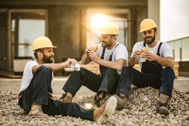 Happy manual workers eating sandwiches on a lunch break at a terrace. Group of happy construction workers having lunch break on a balcony. construction lunch break stock pictures, royalty-free photos & images