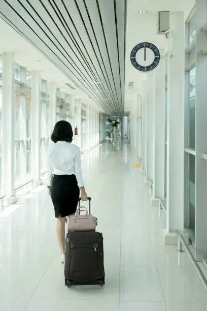 Rear view of young businesswoman carrying a luggage while walking in the train station corridor