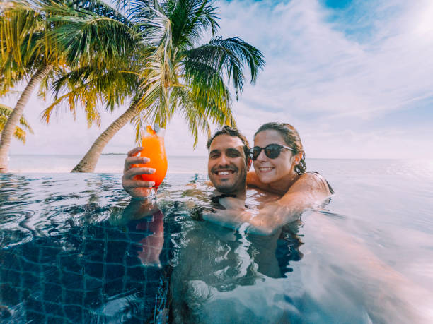 giovane coppia di adulti che fa un selfie in piscina in un'isola paradisiaca - hotel zone foto e immagini stock